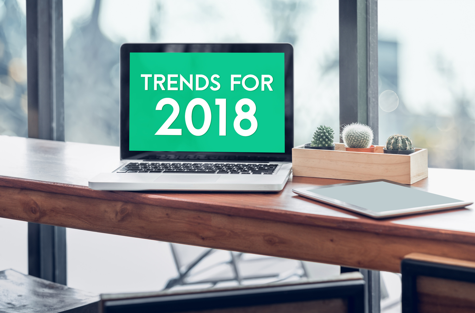 Trends for 2018 word in laptop computer screen with tablet on wood stood table in at window with blur background,Digital Business or marketing trending